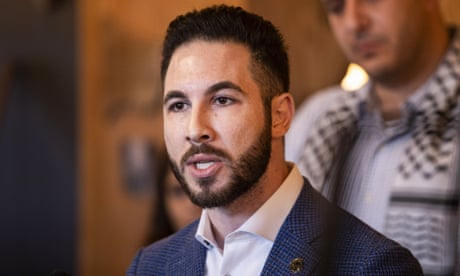 A young man in a blue suit and white shirt speaks.